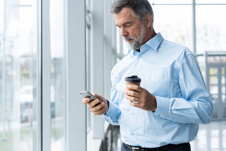 Mature business owner accessing time tracking data report on his phone while having coffee